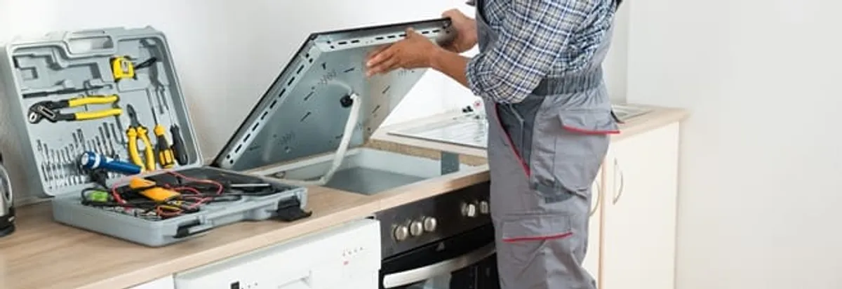 Cooktop repair technician lifting a built-in stovetop for service in Tallahassee, FL