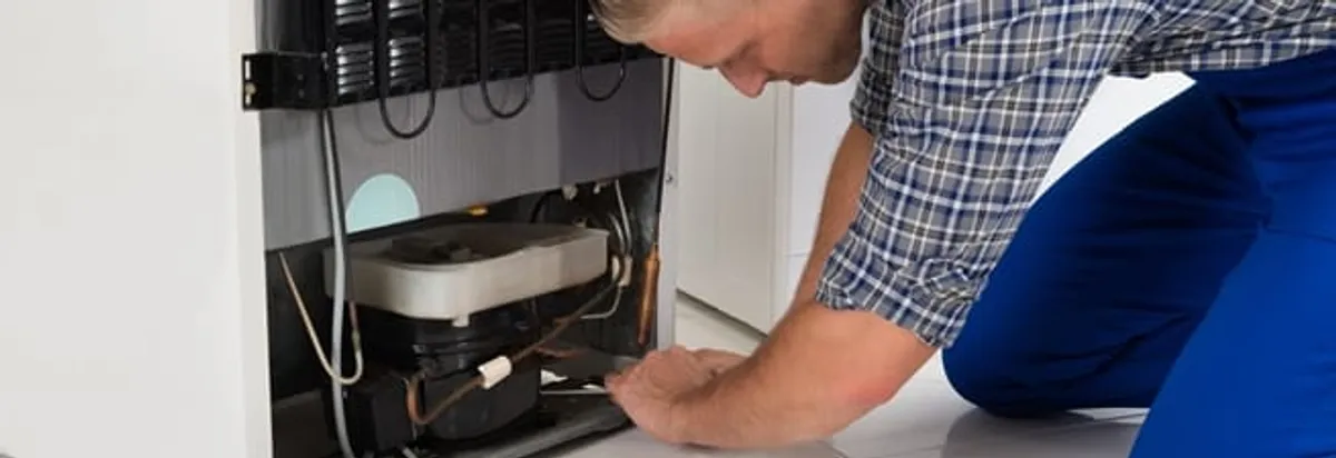 Refrigerator repair technician servicing the compressor and condenser area in Tallahassee, FL